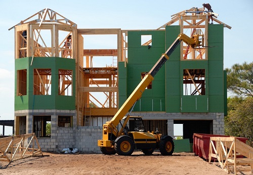 Image of a green building being constructed with a yellow lift sitting in front of the building
