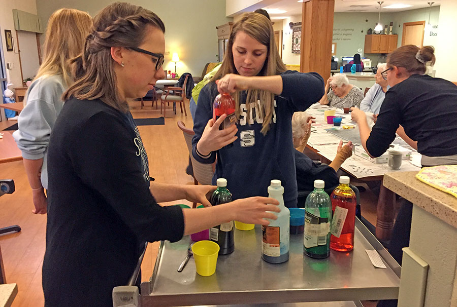 UW-Stout students Leah Wolfe, at left, and Kaitlyn Lee prepare egg dye to color Easter eggs with residents at the Neighbors of Dunn County.