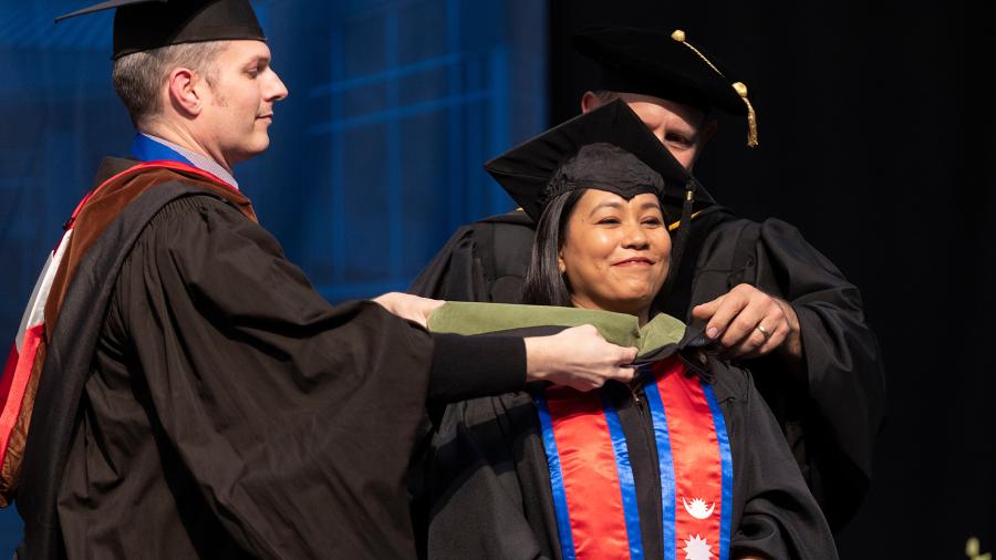 A graduate receives her hood from officials as part of the Graduate School ceremony.