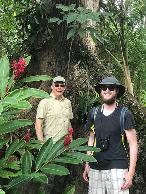 Student Evan Croft, front, and Professor Steve Nold stand in the shadows of a large kapok tree. 